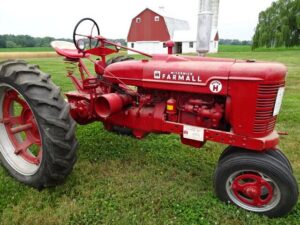Röd veterantraktor av märket Farmall på en gräsmatta framför en lada.